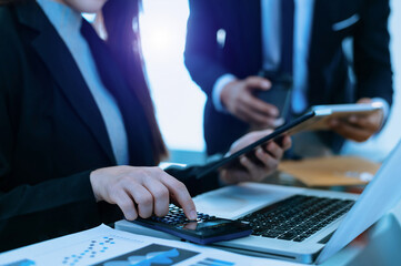 Businessman hand using smartphone, laptop and tablet with social network diagram and two colleagues discussing data on desk as concept