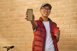 Young cheerful asian male courier with cup of coffee showing scr