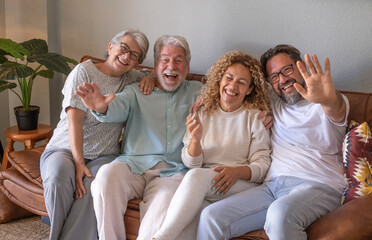 Happy group of family sitting on sofa at home having fun and laughing. Handsome  people, parents and adult sons, two generations looking at camera