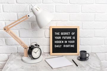 Wall Mural - The secret of your future is hidden in your daily routine. Motivational quote on letter board, alarm clock, lamp on workplace. Concept inspirational quote of the day. Front view