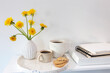 A bouquet of dandelions in a white fluted vase and two cups of different sizes with coffee on a white table.