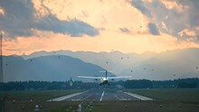 Old passenger airplane landing on the runway against beautiful dramatic sunset at Brnik airport, Slovenia. Aircraft landing. View of long runway and Alps mountains