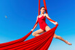 acrobat athletic, graceful gymnast performing aerial exercise with red fabrics outdoors on sky background. flexible woman in red suit performs circus artist dancing in air on silk demonstrates poses.
