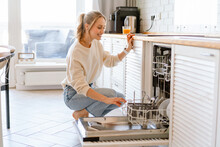Smiling Young White Woman Putting Dishes In The Dishwasher At Home