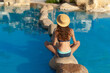© timonko - Woman in hat sits on stone in the middle yoga of the swimming pool spa. Beautiful exotic hotel relax in Egypt. Blue water texture is place for your text