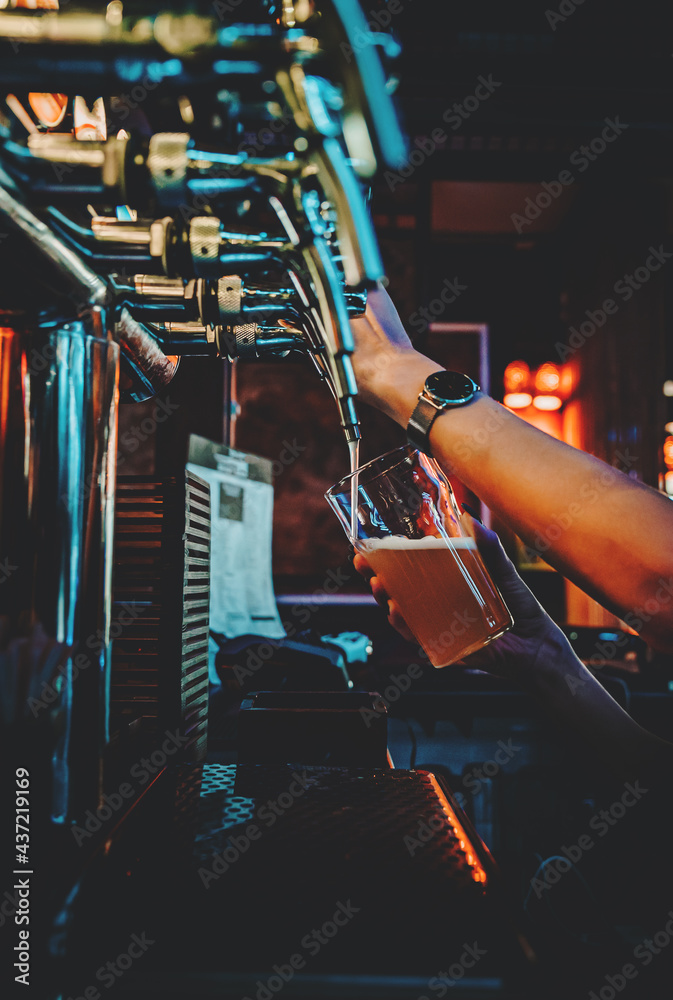 bartender hand at beer tap pouring a draught beer in glass serving in a restaurant or pub - obrazy, fototapety, plakaty 