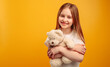 © Ievgen Skrypko - Beautiful little girl child hugging teddy bear and smiling isolated on yellow background with copyspace. Horizontal portrait of kid holding toy and looking at the camera