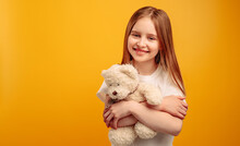 Beautiful Little Girl Child Hugging Teddy Bear And Smiling Isolated On Yellow Background With Copyspace. Horizontal Portrait Of Kid Holding Toy And Looking At The Camera