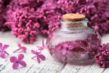 Wall Mural - Bottle of oil or infusion from lilac flowers on white wooden table. 