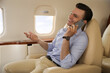 © New Africa - Businessman talking on mobile phone in airplane during flight