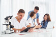 © standret - Man with microscope. Group of young doctors is working together in the modern office