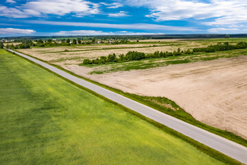 Aerial panoramic view of nature. The road in the fields and dense forest. Fields, meadows, road, outside urban nature in Europe. Blue beautiful sky and white clouds. Natural landscape, summer. 