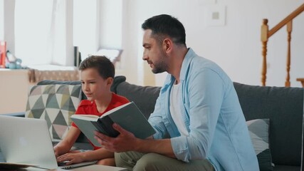 Wall Mural - Father helping his son with homework while sitting on the couch in the living room