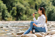 Attractive woman drinking red wine sitting on a rock in the riverside.