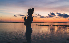 Side Silhouette View Of Calm Girl In Sportive Clothing Praying And Meditating For Getting Soul Inspiration, Woman In Namaste Thinking About Harmony And Mindfulness Recreating At Evening Seashore