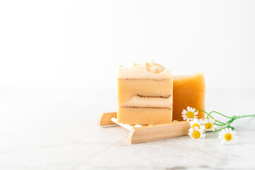 Homemade Soap with chamomile Flowers in wooden soap dish on white marble background. Zero waste, natural organic bathroom cosmetics. Plastic free life. Ecological skin care, body treatment concept