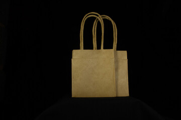 two overlapping mini recycled brown paper bags with paper handles isolated on a black background