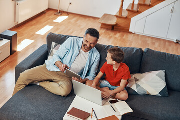 Wall Mural - Top view of happy young father helping his son with homework while homeschooling in the living room