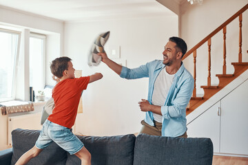 Wall Mural - Happy young father and son having pillow fight and smiling while spending time at home