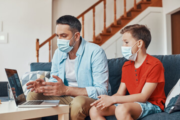 Wall Mural - Father and son using laptop to have a video call with doctor while spending time at home