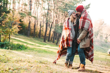 Wall Mural - Couple huggings travelers covered with plaid in the forest. Concept of trekking, adventure and seasonal vacation.