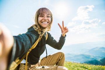 young woman taking selfie portrait hiking mountains - happy hiker on the top of the cliff smiling at