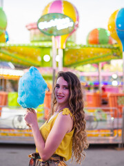 Wall Mural - Vertical shot of an attractive Caucasian female posing with blue cotton candy at a carnival