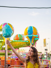 Wall Mural - Vertical shot of an attractive Caucasian female posing with blue cotton candy at a carnival