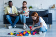 multiethnic couple sitting on couch with infant near preteen daughter playing with building blocks