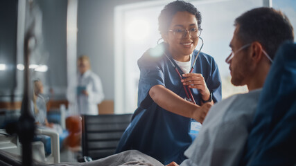 Wall Mural - Hospital Ward: Friendly Black Head Nurse Uses Stethoscope to Listen to Heartbeat and Lungs of Recovering Male Patient Resting in Bed, Does Checkup. Man Getting well after Successful Surgery