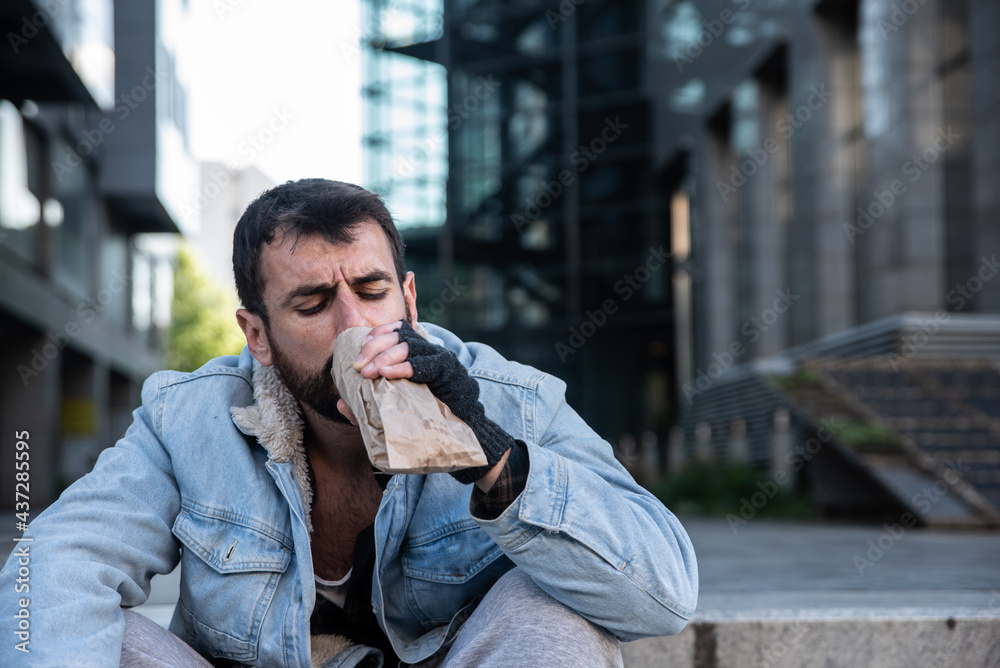 Young depressed sick alcoholic homeless man sitting alone on the street ...