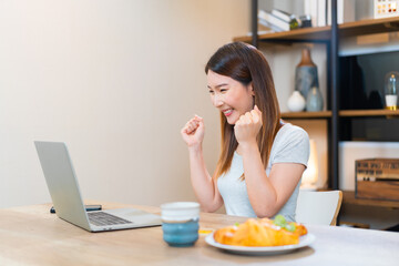 Asian woman using laptop and typing keyboard work at home. Happy female success job or win online game. excitement, successful concept.