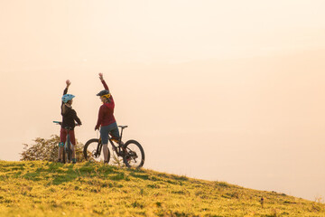 Two happy woman high five over the sunset after a successful mountain biking trip in the mountains. Celebrate a cross country cycling journey.