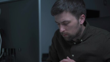 Tired male working on computer. Sad exhausted man at home office. Stressful work, stress at workplace. Software developer looks very tired during completion overtime of project, working on computer