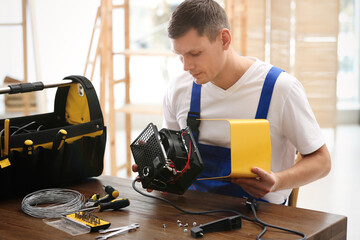 Wall Mural - Professional technician repairing electric fan heater at table indoors