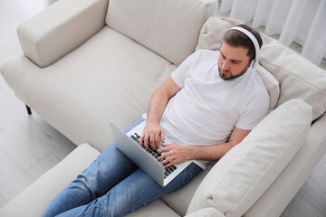 Wall Mural - Man with laptop and headphones sitting on sofa at home