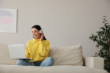 Wall Mural - Woman with laptop and headphones sitting on sofa at home