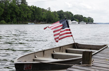 American Flag Blowing In The Wind On An Old Aluminum Boat Floating On The River