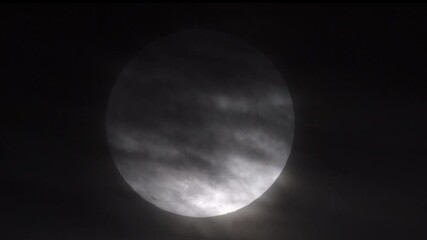zoomed in view of a super full moon with eerie, wispy clouds partially obscuring it