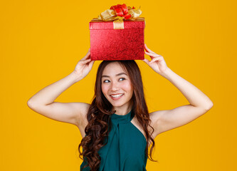 Happy smile face cute Asian girl with dark hair holding gift box over head  with delightful and excited, studio shot on yellow background. Celebrate and festival concept