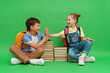 Two happy schoolboys in loose clothes sit on stacks of school books and read books and cheerfully smile and give each other a high five, on a green background. The concept of parenting. Back to school