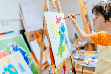 Close up shot of caucasian boy with Down's syndrome painting with easel in art class at school. Concept disabled kid learning.