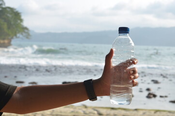  male hand holding water mineral bottle with blurred beach or sea background