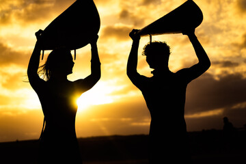 Silhouette of surfer people carrying their surfboards on sunset beach. Sport and friendships concept.