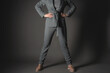 © Natali - Confident business woman is standing with her arms on her belt on a gray background.