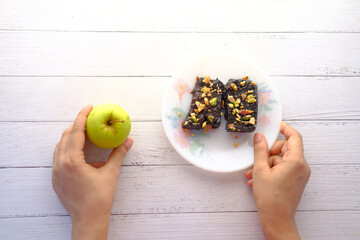 Wall Mural -  hand hold apple and brownie on plate on table 