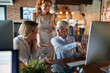 © luckybusiness - A senior business woman is showing a content on a computer screen to her female colleagues at the workplace. Business, office, job