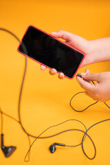 Poster - Vertical shot of a person plugging earphones to a mobile phone isolated on a yellow background