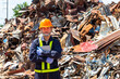 A worker at a recycling plant stands in a pile of scrap metal holding a tablet.