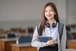 © EduLife Photos - Portrait of young Asian woman student in uniform holding tablet in smart and happy pose in university or college classroom. Youth girl student and tutoring education with technology learning concept.